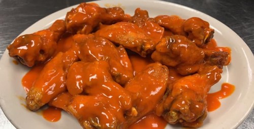 A plate of spicy chicken wings coated in bright red hot sauce.