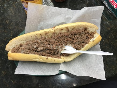 A halved sandwich filled with shredded beef, served on a white roll with a plastic fork on a paper-lined plate.