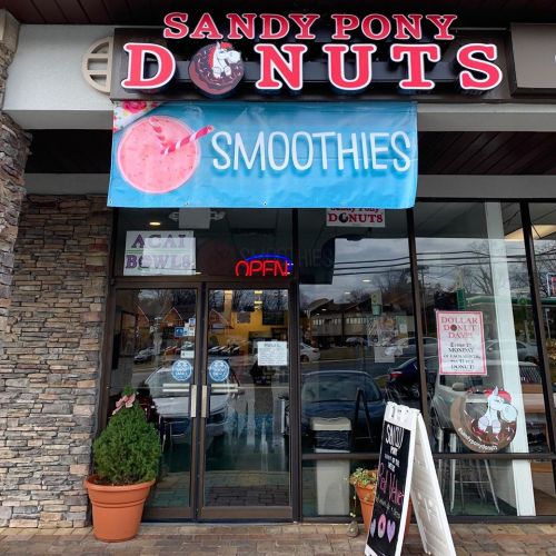 Exterior of Sandy Pony Donuts featuring a sign for smoothies and a welcoming entrance with potted plants.