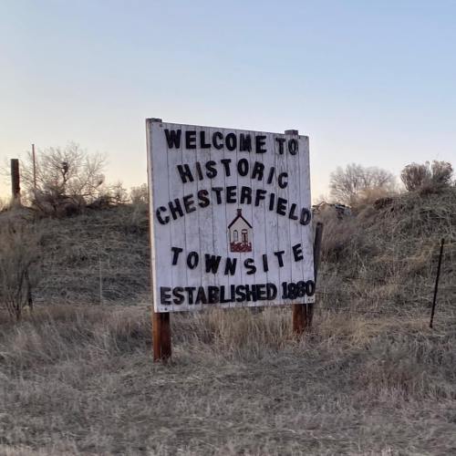 Sign welcoming visitors to Historic Chesterfield Townsite, established in 1880, surrounded by dry grass and shrubs.