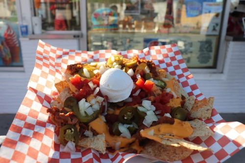 A plate of nachos topped with cheese, jalapeños, tomatoes, onions, and a dollop of sour cream, set against a colorful background.