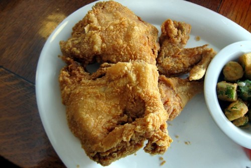 A plate with two pieces of golden-brown fried chicken and a small bowl of fried okra on the side.