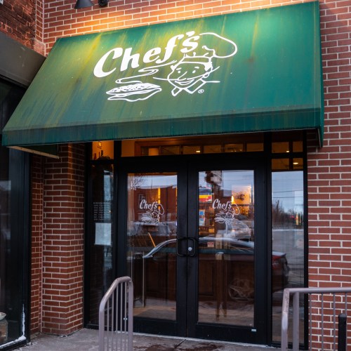 Green awning with "Chef's" logo over glass double doors of a brick restaurant entrance.
