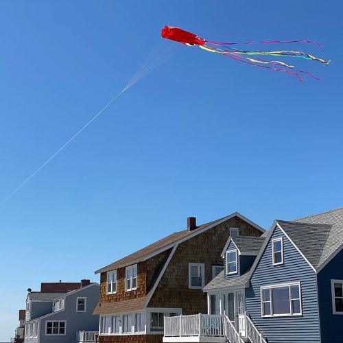 A colorful kite shaped like a jellyfish flies above beach houses against a clear blue sky.