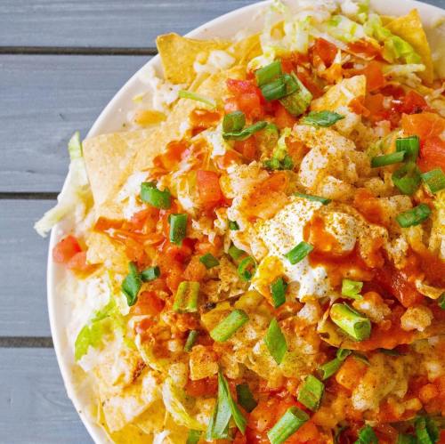 A plate of nachos topped with cheese, tomatoes, lettuce, green onions, and a drizzle of sauce.