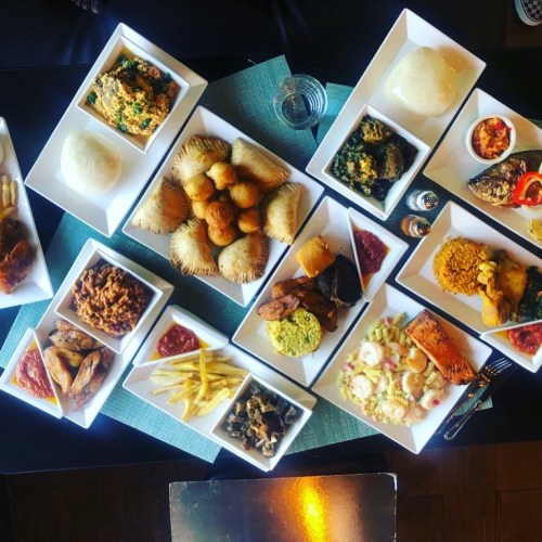 A variety of dishes served in white bowls, including rice, fish, meat, and pastries, arranged on a table.