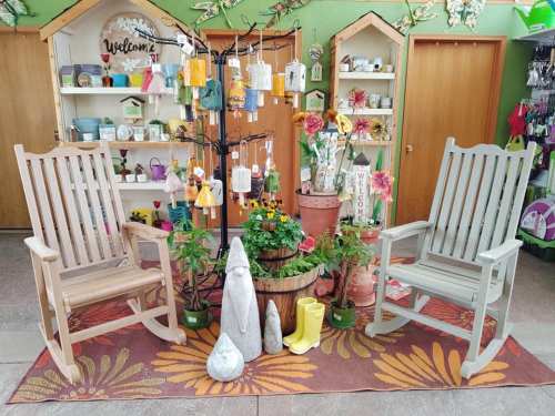 Two rocking chairs flank a potted plant display, surrounded by garden decor and colorful wind chimes in a cozy shop.