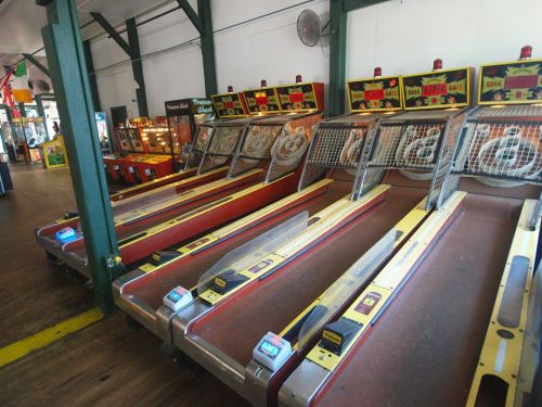 A row of vintage skee-ball machines in a game arcade, with colorful designs and wooden flooring.