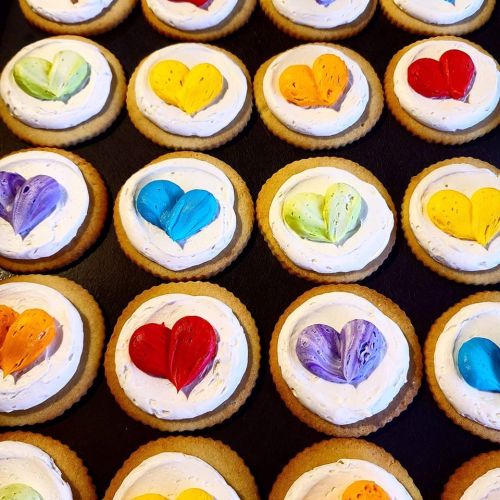 A tray of cookies topped with colorful heart-shaped icing on a creamy frosting base.