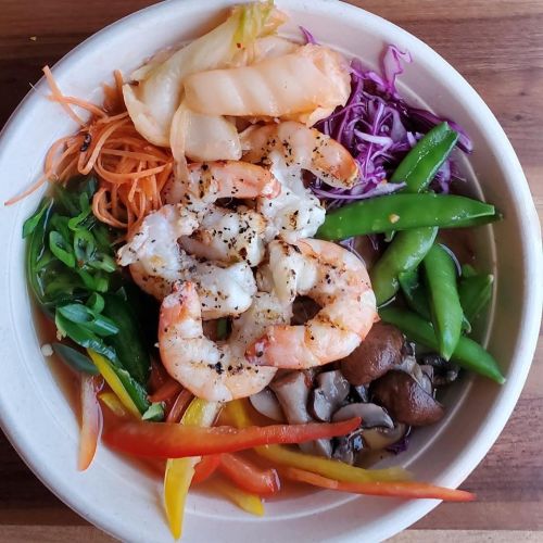 A bowl filled with shrimp, colorful vegetables like carrots, bell peppers, and cabbage, arranged beautifully.