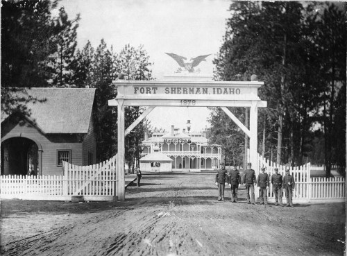 Historic photo of Fort Sherman, Idaho, featuring soldiers in uniform at the entrance gate, surrounded by trees.