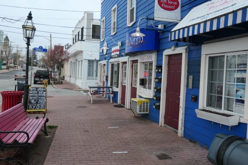 A colorful blue building with shops, a bench, and a sign on the sidewalk in a small town setting.