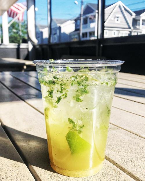 A refreshing drink with mint and lime in a clear cup, set on a wooden table with a sunny outdoor background.