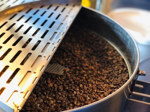 Close-up of a coffee roaster with roasted coffee beans inside, lid partially open, revealing the rich brown beans.