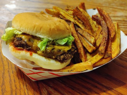 A juicy cheeseburger with lettuce on a bun, served with a side of crispy seasoned fries in a paper tray.