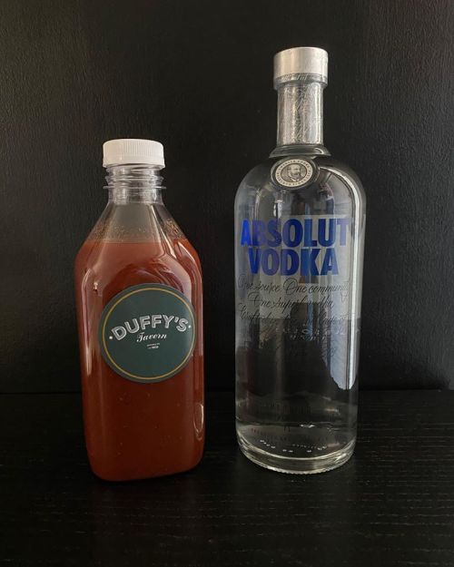 A bottle of Duffy's hot sauce next to a bottle of Absolut vodka on a dark background.