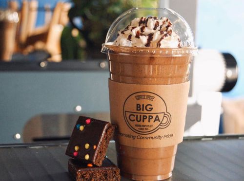 A frosty chocolate drink topped with whipped cream and chocolate drizzle, next to a brownie with colorful sprinkles.
