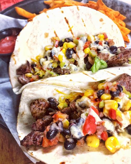 Two tacos filled with beef, black beans, corn, tomatoes, and cheese, served with sweet potato fries and salsa.