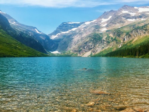 A serene lake surrounded by mountains, with clear blue water and a bright sky, reflecting the natural beauty of the landscape.