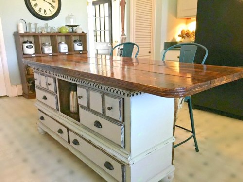 A rustic kitchen island with a wooden top, drawers, and a light-colored base, set in a bright, airy kitchen.