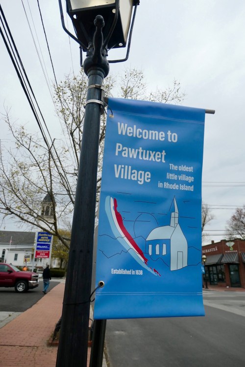 Blue banner on a lamp post reads "Welcome to Pawtuxet Village," featuring a church graphic and establishment year 1538.