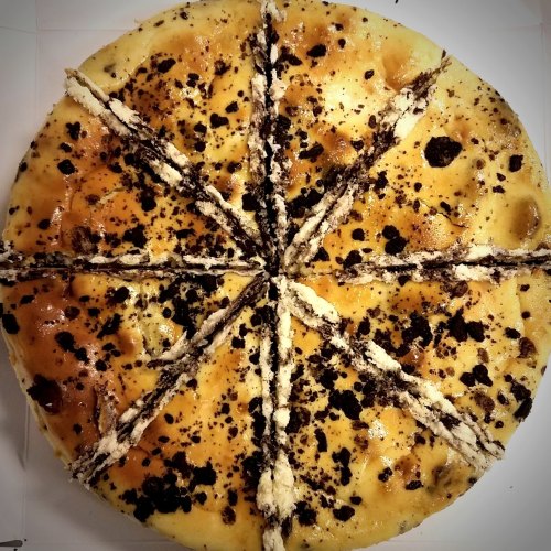 A round cheesecake topped with crushed cookies, sliced into 12 pieces, showcasing a creamy texture and golden crust.