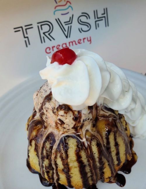 A decadent dessert featuring a cake topped with ice cream, chocolate sauce, whipped cream, and a cherry.
