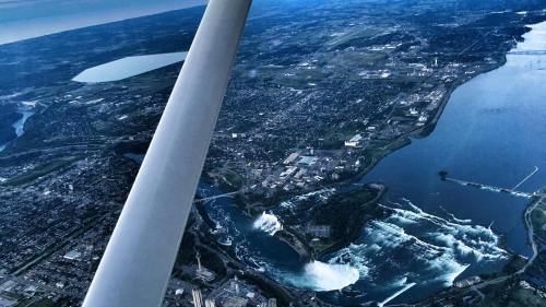 Aerial view of a city near a large waterfall, with rivers and green landscapes visible in the background.