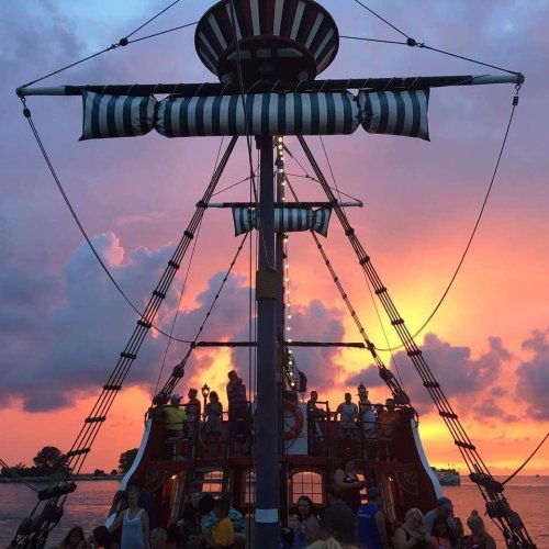 A pirate ship silhouette against a vibrant sunset, with people enjoying the view on deck.