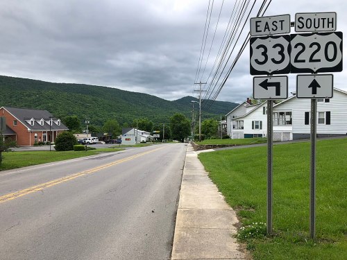 Road sign indicating East 33 and South 220 directions, with a view of a quiet street and mountains in the background.