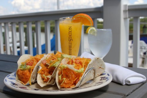 Three tacos filled with shredded lettuce and cheese, served with a colorful drink and a glass of water on a table.