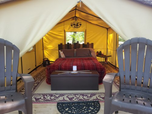 Cozy tent interior with a bed, two chairs, and decorative elements, creating a warm and inviting atmosphere.