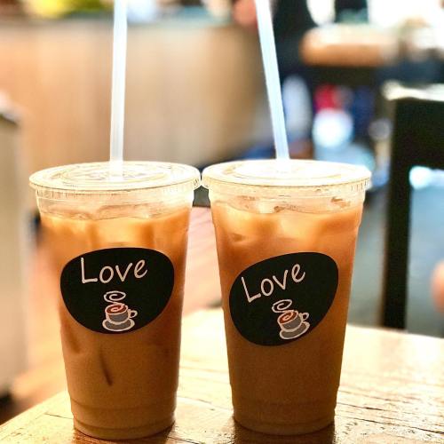 Two iced coffee cups with "Love" stickers, sitting on a wooden table in a cozy café setting.