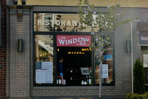 A restaurant window displays "The Window at Basta" sign, with a person inside and bottles visible on the counter.