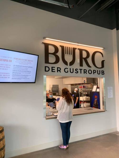 A customer orders at the counter of "Burg Der Gastropub," with staff in the background wearing masks.