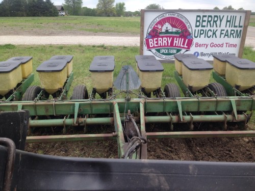 Close-up of a green farming planter with yellow seed boxes, next to a sign for Berry Hill U-Pick Farm.