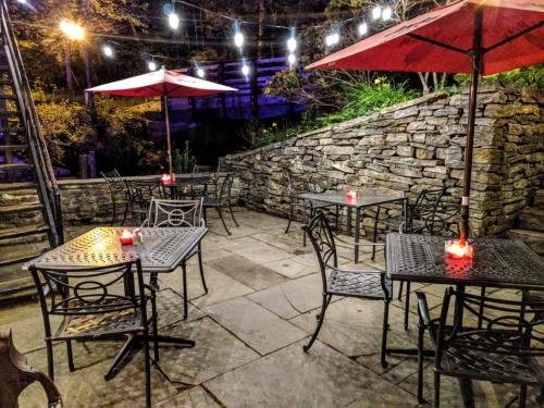 Outdoor dining area with stone walls, tables, and red umbrellas, illuminated by string lights and candles.