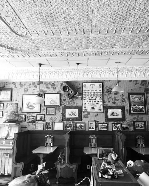 A vintage-style café interior with patterned ceiling, wooden booths, and walls adorned with framed art and memorabilia.