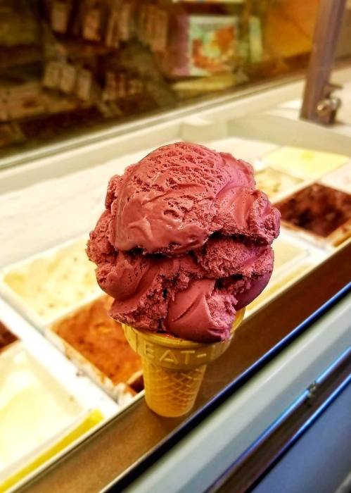 A close-up of a cone topped with rich purple ice cream, with various flavors visible in the background.