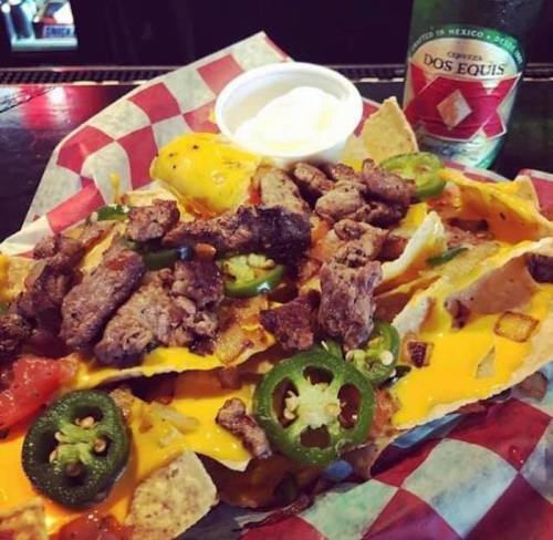 A plate of nachos topped with beef, jalapeños, cheese, and a side of sour cream, alongside a bottle of Dos Equis beer.