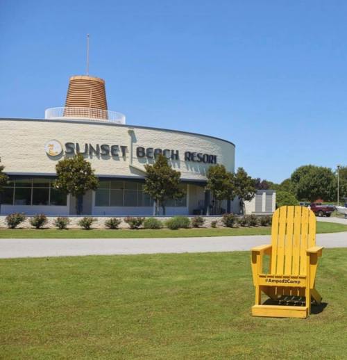 A large yellow Adirondack chair in front of the Sunset Beach Resort building on a sunny day.