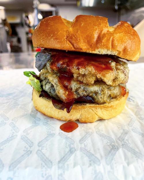 A close-up of a stacked burger with crispy layers, lettuce, and sauce, served on a toasted bun.