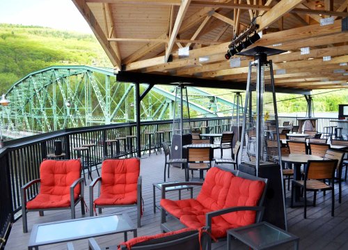 A cozy outdoor seating area with red chairs and a view of a green bridge in a scenic landscape.