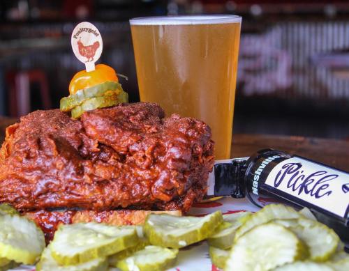 A plate of spicy fried chicken topped with pickles and a drink, served with sliced pickles on the side.