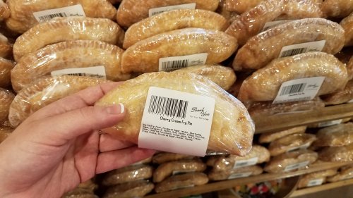 A hand holding a packaged cherry cream fry pie in front of a display of similar pies.