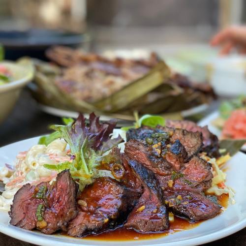 A plate of grilled steak slices drizzled with sauce, garnished with greens, and accompanied by a side of salad.