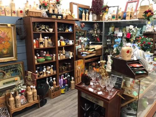 A cozy shop filled with vintage items, including bottles, glassware, and decorative pieces on shelves and tables.