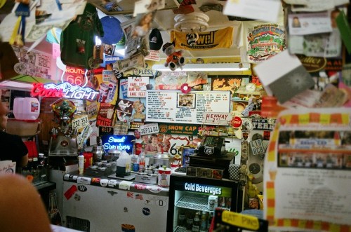 A cluttered bar interior filled with vintage signs, memorabilia, and a neon "Cold Beverages" sign.