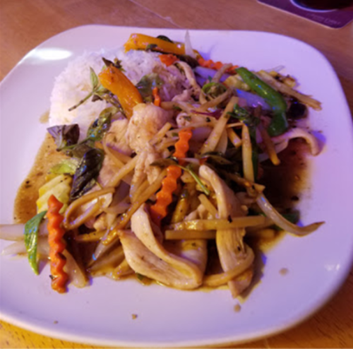 A plate of stir-fried vegetables and chicken served with rice, featuring colorful peppers and herbs.