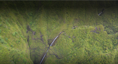 Aerial view of lush green mountains with a waterfall cascading down a steep valley.